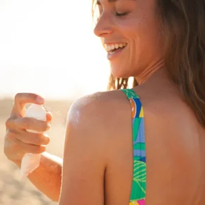 En mann kledd i lette sommerklær bruker Acorelle SPF 50 solspray på ansiktet før en dag på stranden i Norge